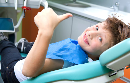 young child giving thumbs up while sitting in dental chair 