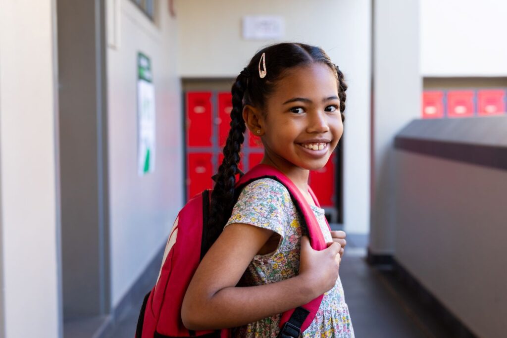 A young girl wearing a backpack in a school hallway.