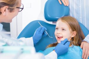 little girl smiling in the chair as the dentist inspects her mouth